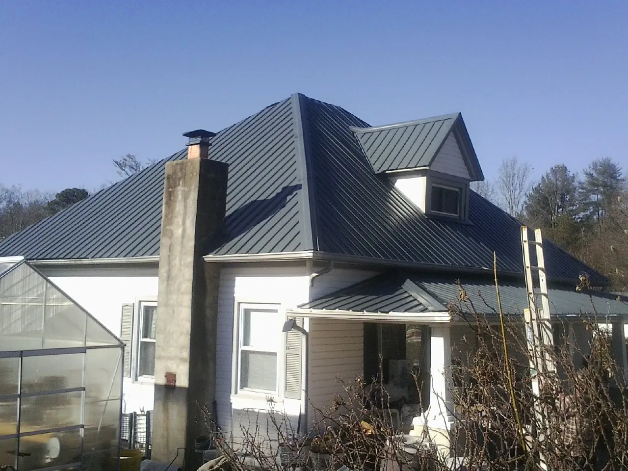 Dark blue standing seam metal roof on a white farmhouse with dormer — Slate & Tile Roof Repair by Roofing Brothers in Rock Valley