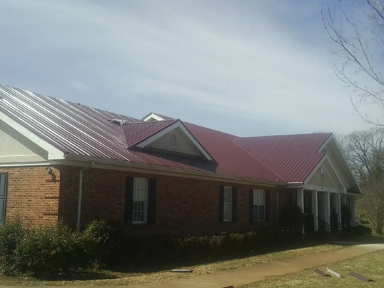 Red metal roof with gabled entries on a long brick building, from a Hail Damage Roof Repair job in Rock Valley