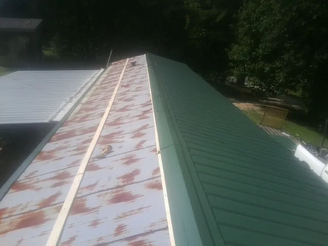 Old rusted panels beside newly installed green metal roofing — Wind Damage Roof Repair by Roofing Brothers in Rock Valley