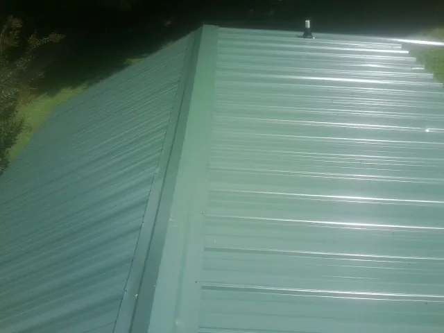 New green metal panels meeting at the ridge of a roof — Flat Roof Repair work by our crew in Rock Valley