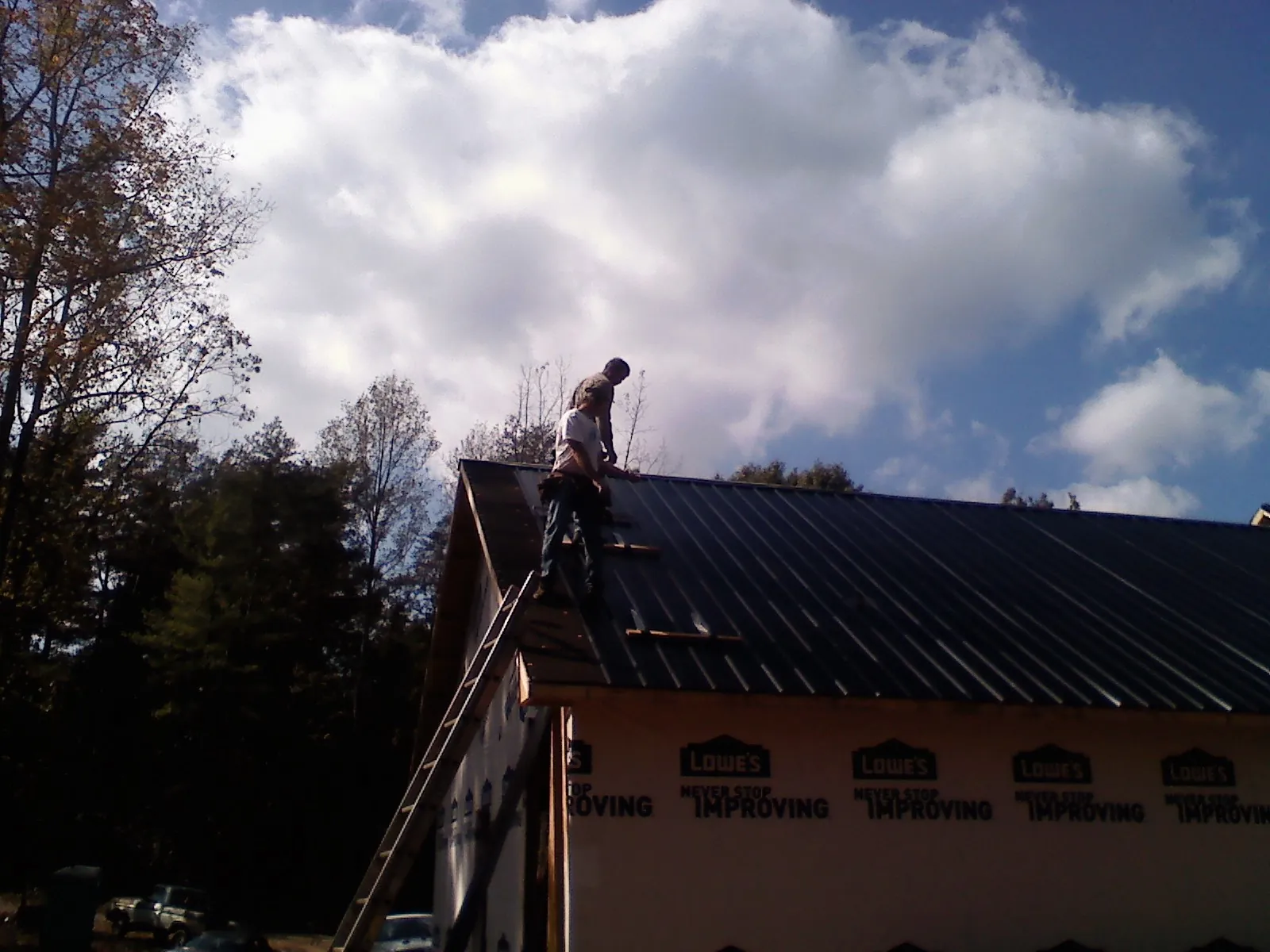 Roofer fastening dark metal panels high against a cloudy sky, from a Roof Inspection job in Rock Valley