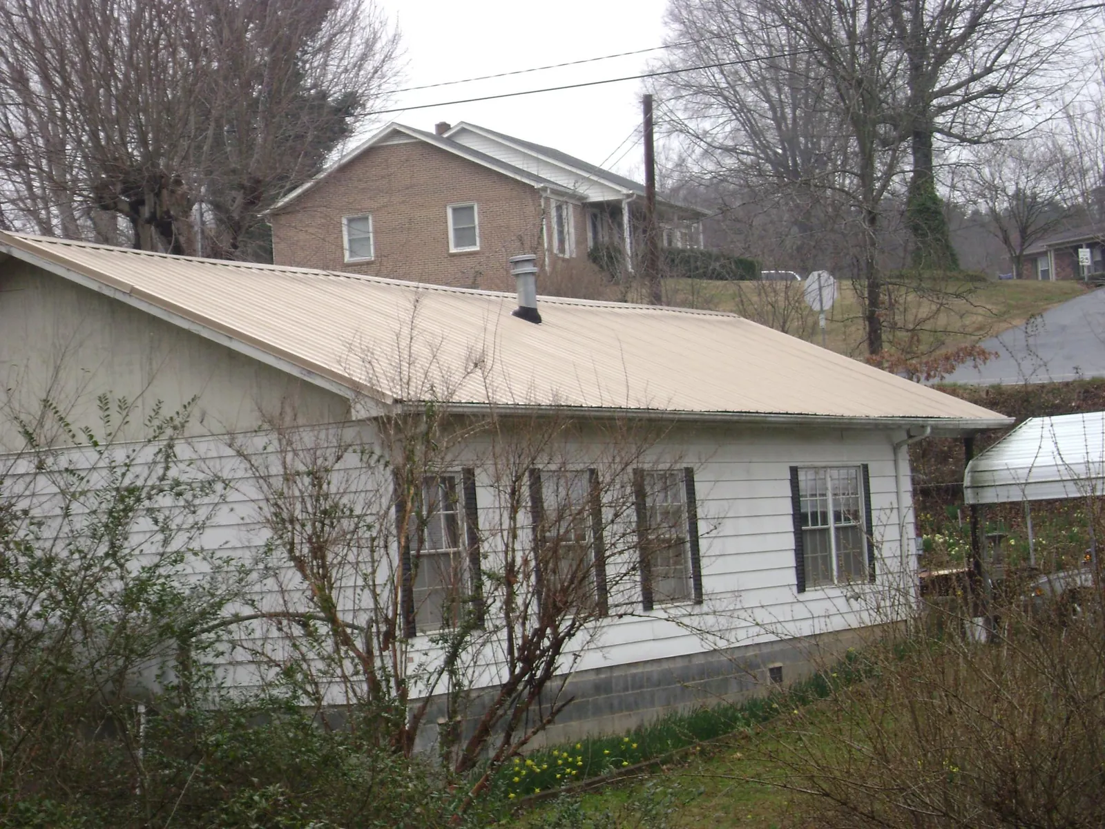 Tan metal roof on a white sided house set into a hillside — Commercial Roofing by Roofing Brothers in Rock Valley